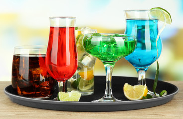 Many glasses of cocktails on tray on table, on bright