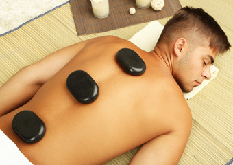 Obraz na płótnie Canvas Young man relaxing with hot stones on back before massage
