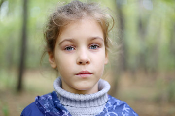 Serious little caucasian girl looks at distance in autumn forest