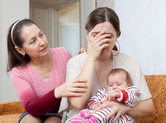 Mature woman comforts crying daughter with baby