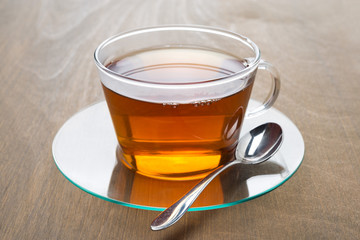 Transparent cup of black tea on wooden background