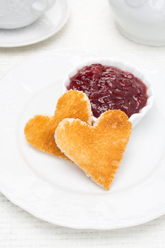 Two toast bread in the shape of hearts and berry jam in a bowl