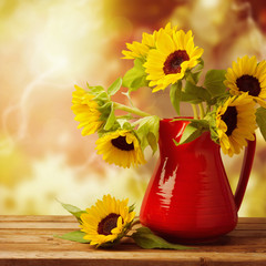 Naklejka premium Sunflower bouquet in jug on wooden table over autumn bokeh