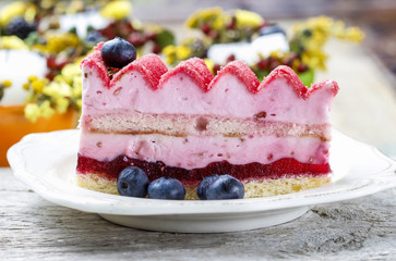 Pink layer cake decorated with fresh fruits on wooden table