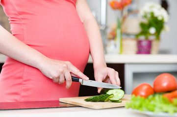 Obraz na płótnie Canvas Close up pregnant woman with knife on kitchen cuts cucumber