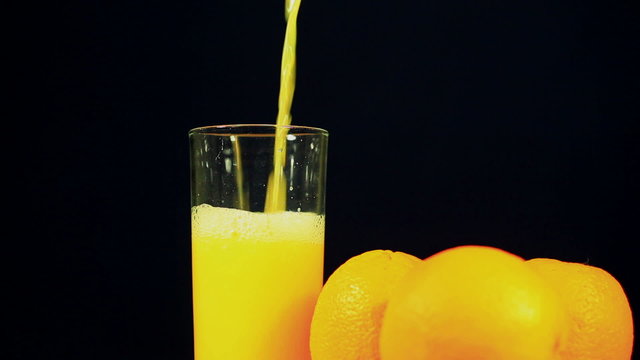 Three oranges and  juice which is pouring in  glass
