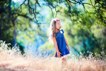 Happy little girl in rye field at summer day trees background