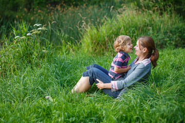 Naklejka na ściany i meble Little boy and his mother sitting on grass in summer forest