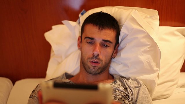 Man reading on his tablet lie down on bed