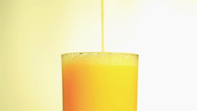 Bright orange juice flowing in a glass close up