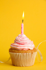 tasty birthday cupcake with candle, on yellow background