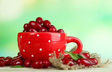 Fresh cornel berries in red cup on wooden table