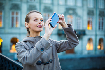 Elegant, young woman taking a photo with her cell phone camera