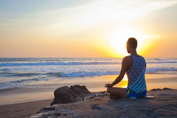 sitting man doing yoga on shore of ocean