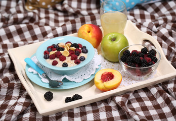 Oatmeal in plate with berries on napkins on wooden tray on bad