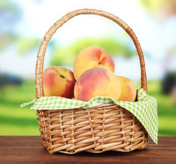 Ripe sweet peaches in wicker basket, on bright background