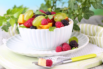 Fruit salad in bowl, on wooden table, on bright background