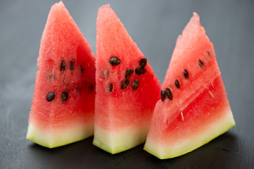 Three slices of ripe watermelon on dark wooden background