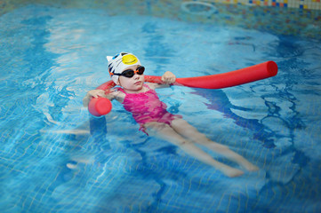 Little girl learning to swim with pool noodle