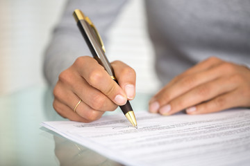 Woman at office desk signing a contract with shallow focus on si