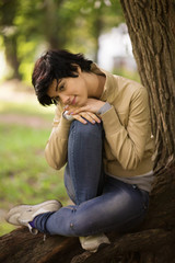 The girl sits in park at a tree