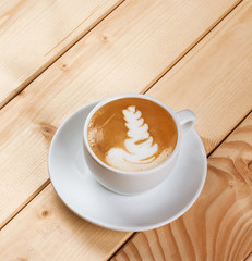 Cappucino with leaf shape foam on wooden table