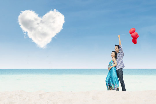 Asian couple enjoy holiday at beach under heart cloud