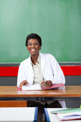 Happy Teacher Looking Away While Sitting With Binder At Desk