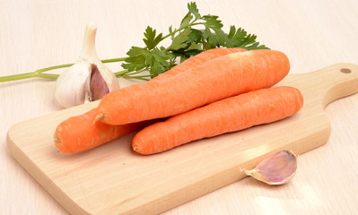 Carrots on a board, garlic, parsley on a table in bright kitchen