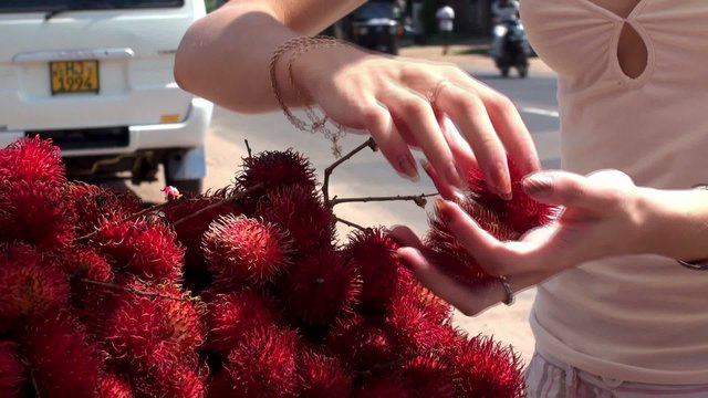 The girl buys a rambutans in a street market.