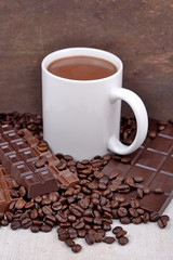 White cup of hot chocolate on coffee beans and chocolate backgro