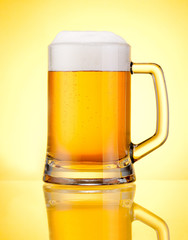 Mug fresh beer with cap of foam isolated over yellow background