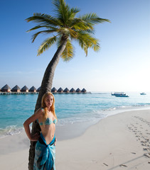 Young beautiful woman stands near palm tree, Maldives