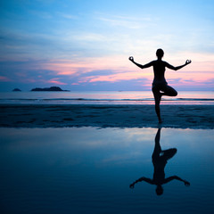 Woman practicing yoga on the beach after sunset.