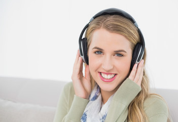 Cheerful cute blonde listening to music sitting on cosy sofa