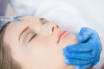 Surgeon making injection on forehead on content woman lying