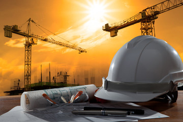 safety helmet and architect pland on wood table with sunset scen