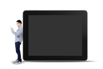 Young man using a mobile phone and standing next to big tablet