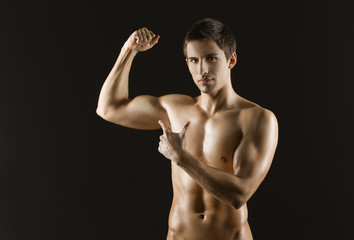Fototapeta premium Naked sportsman pointing at his bicep, isolated on black