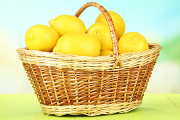 Ripe lemons in wicker basket on table on bright background