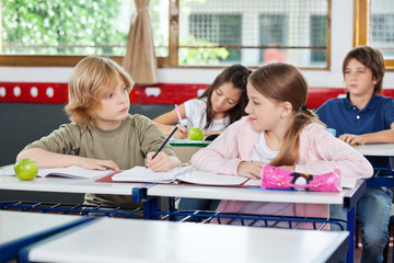 Fototapeta premium Schoolboy Looking At Girl While Writing At Desk