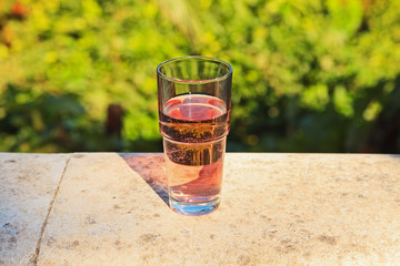Glass of fresh pink soda on balcony with blurred green garden ba