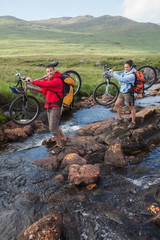 Couple crossing a stream holding their mountain bikes