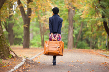 Redhead girl with suitcase at autumn outdoor.