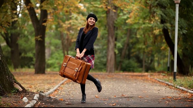Redhead girl with suitcase at autumn outdoor.