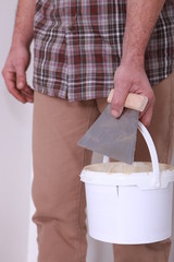 Man holding bucket of plaster and trowel