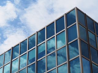 Wolken spiegeln sich in der Glasfassade eines modernen Bürogebäudes