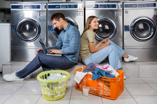 Couple Using Laptop And Earphones At Laundry - Powered by Adobe