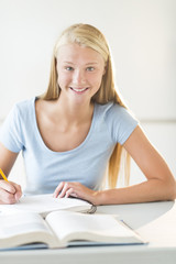 Happy Teenage Student Sitting At Desk In Classroom