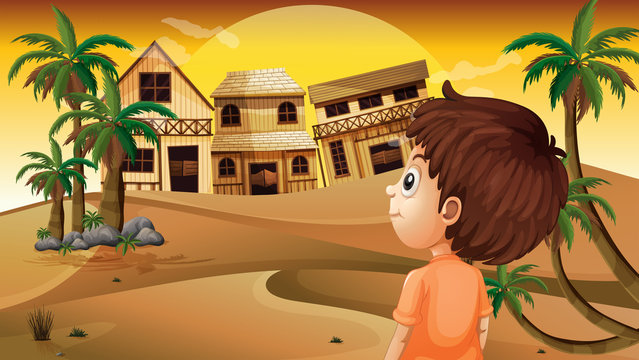 A boy at the desert standing in front of the wooden houses